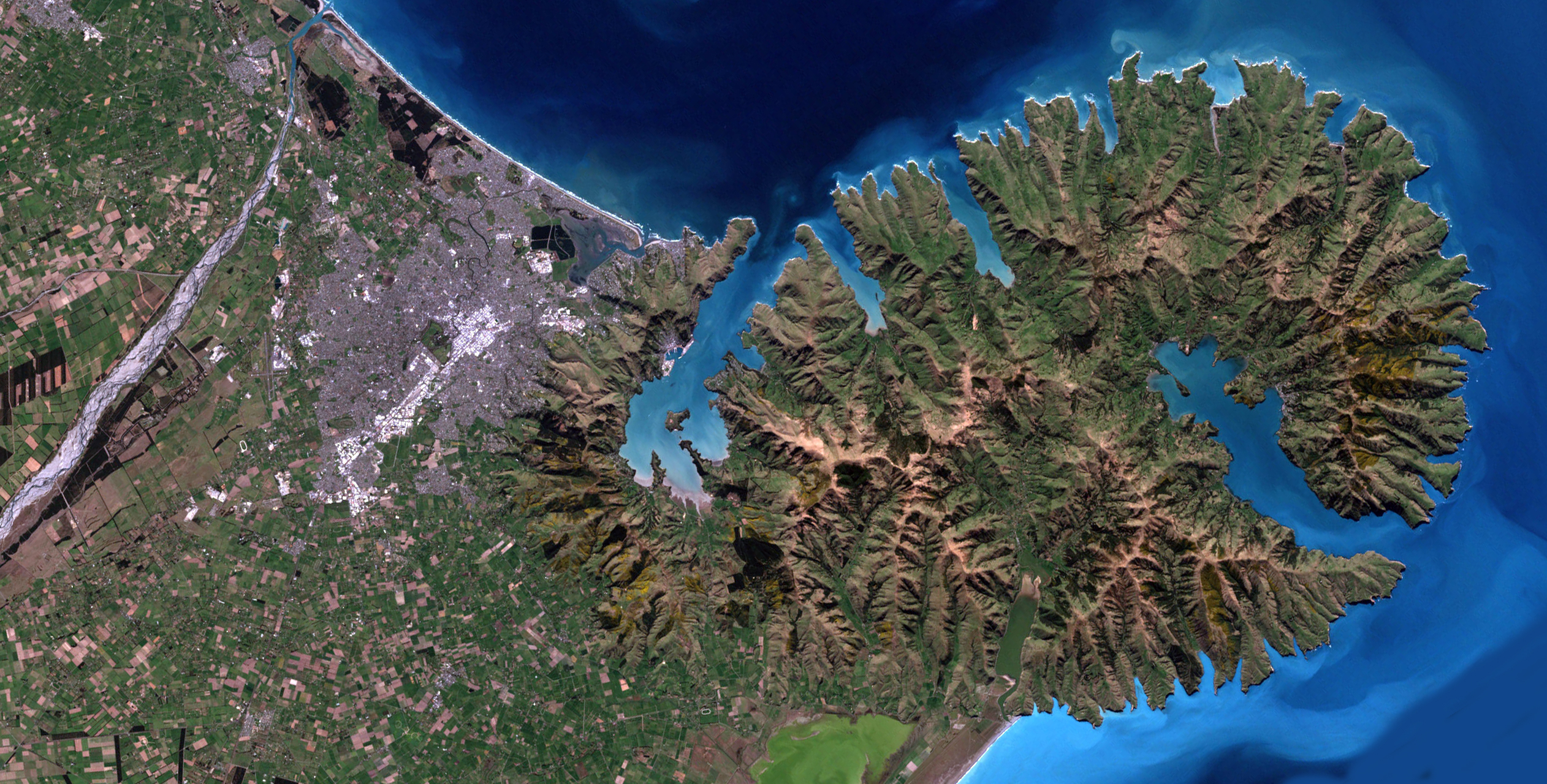This satellite image shows Banks Peninsula, including Lyttelton Harbour and Akaroa Harbour, and the city of Christchurch, in Canterbury, New Zealand.