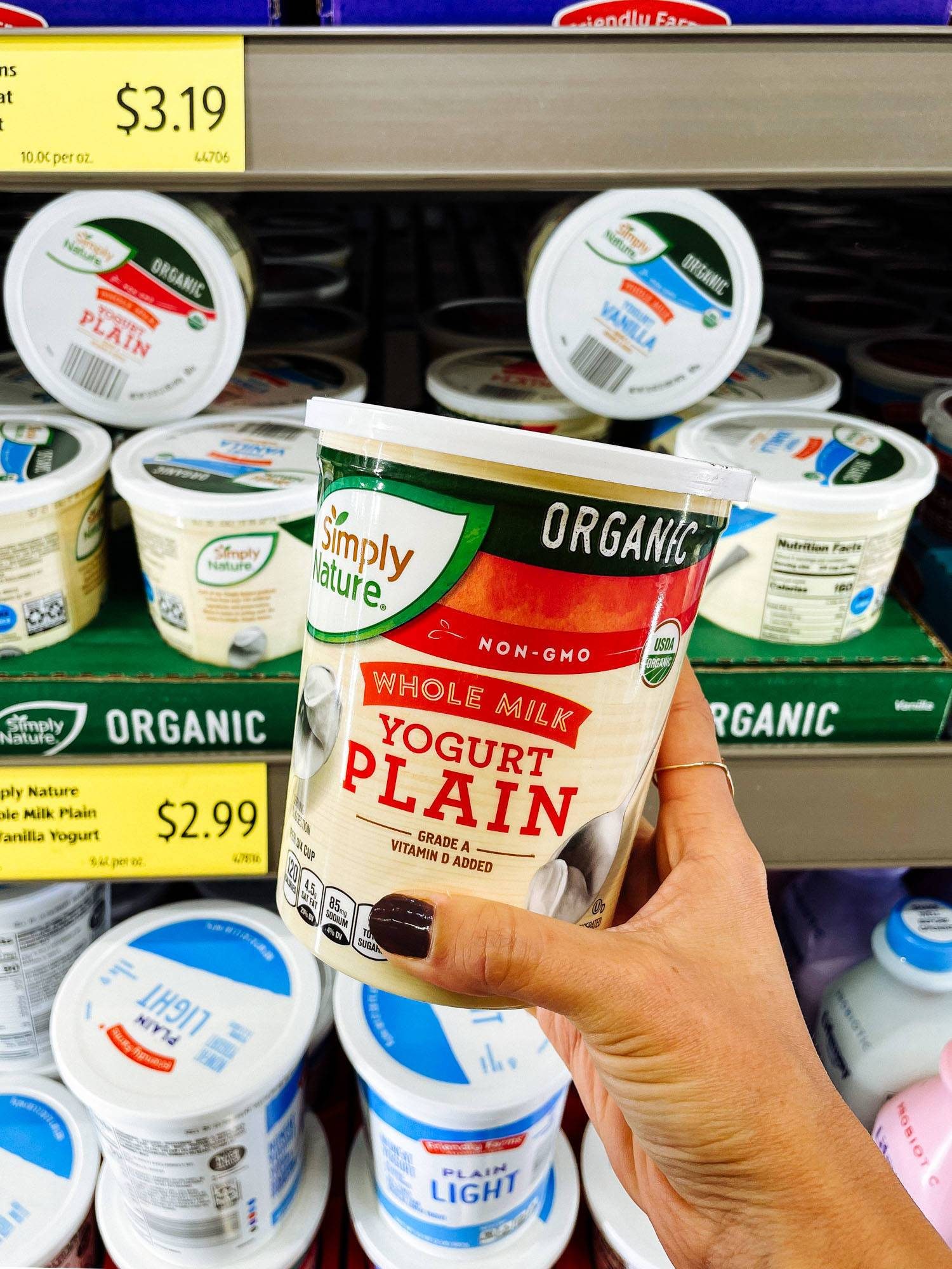White hand holding organic plain yogurt from ALDI.