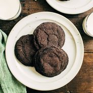 Dark chocolate cookies on a plate next to a glass of milk.